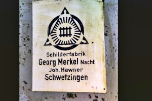 Aufkleber der Firma auf der Rückseite eines Leuchttransparentes, welches halbwegs zugänglich war. Der Aufkleber wurde für das Foto von Grünspan befreit.